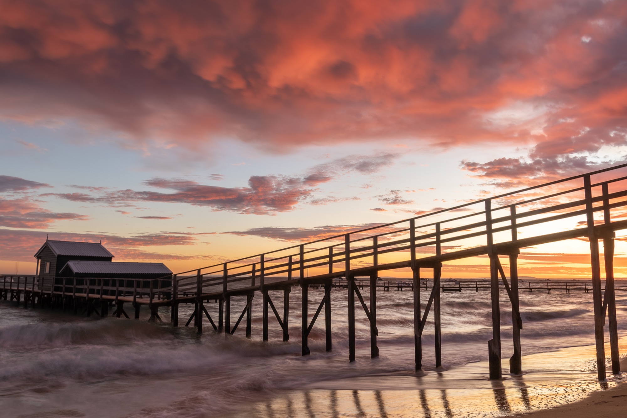 Wooden pier reaching into a stormy red sunset.