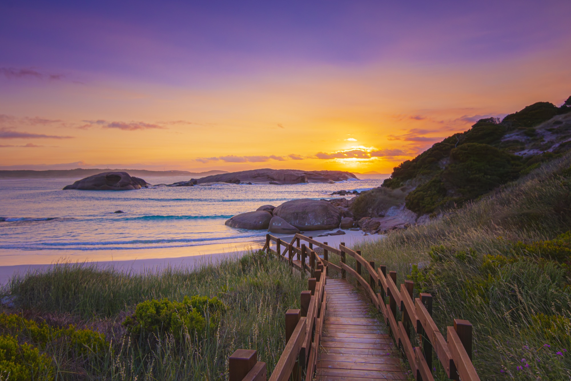 Wooden boardwalk leading down to a beach at sunset.